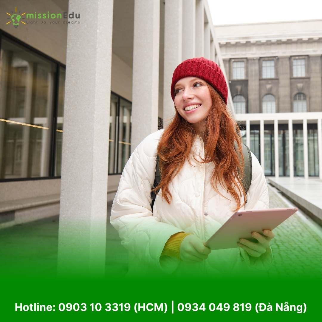 Nữ sinh viên tóc đỏ mặc áo khoác trắng, dùng iPad trước ký túc xá đại học.