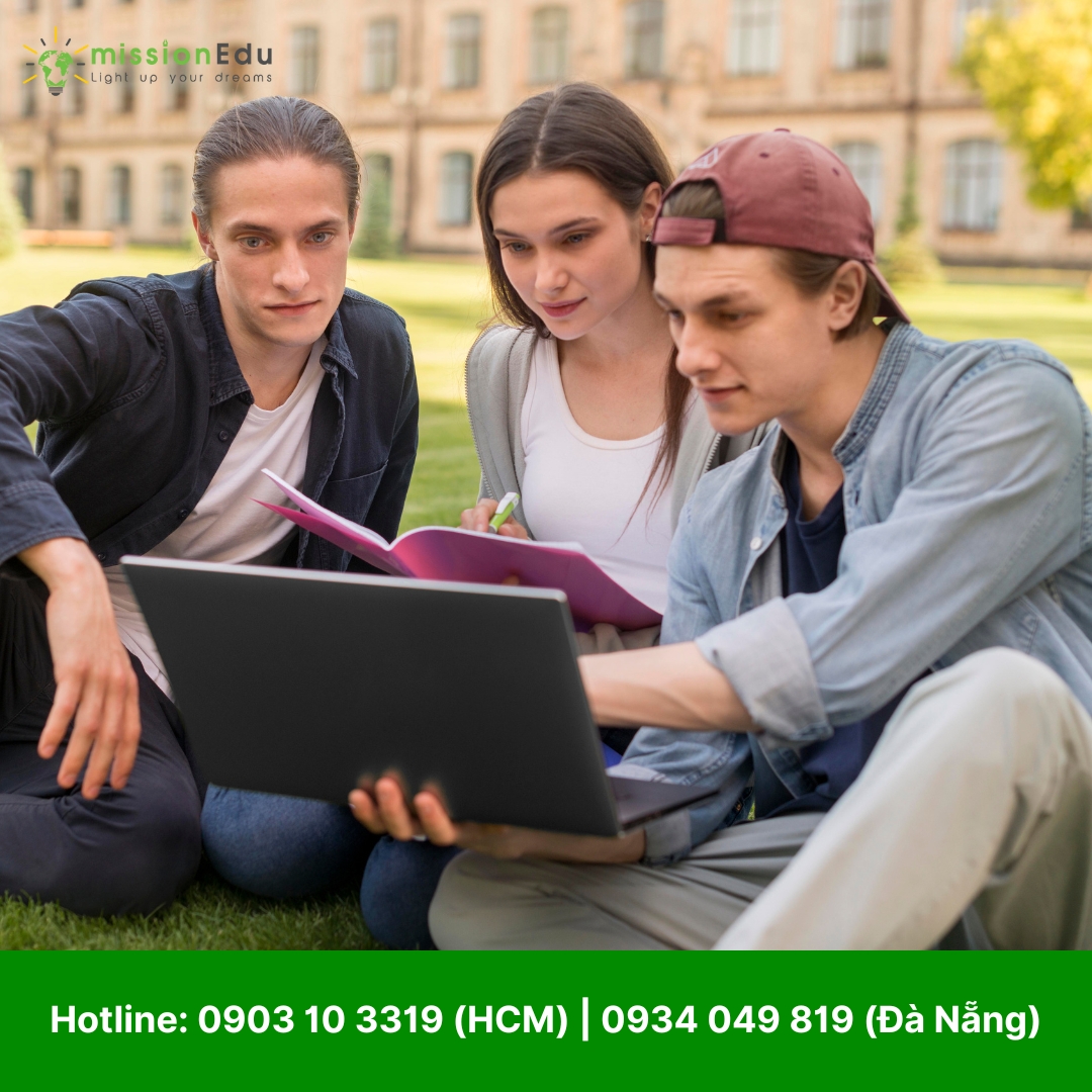 Ba sinh viên đại học đang ngồi trên cỏ, học nhóm. Một nam sinh và một nữ sinh đang chăm chú nhìn vào màn hình máy tính xách tay do một nam sinh khác đang sử dụng. Họ đang thảo luận bài học, với sách và vở ghi đặt bên cạnh.